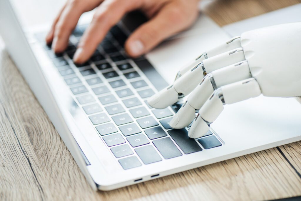 Image description: close-up view of human and robot hands typing on laptop at workplace