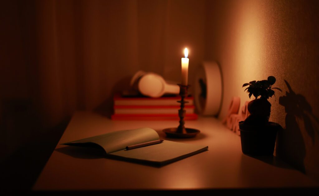 Just avoid these common home office lighting mistakes. Image description: In the dark room, burning candle in candlestick is lighting on the work desk where the paper