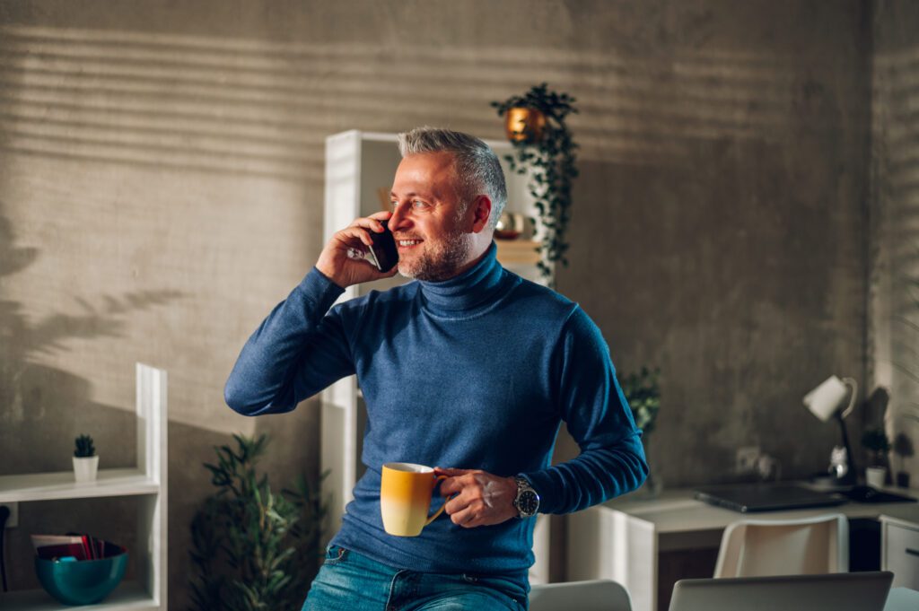 Middle aged man using smartphone and drinking coffee at home. Mastering time can free up your time.