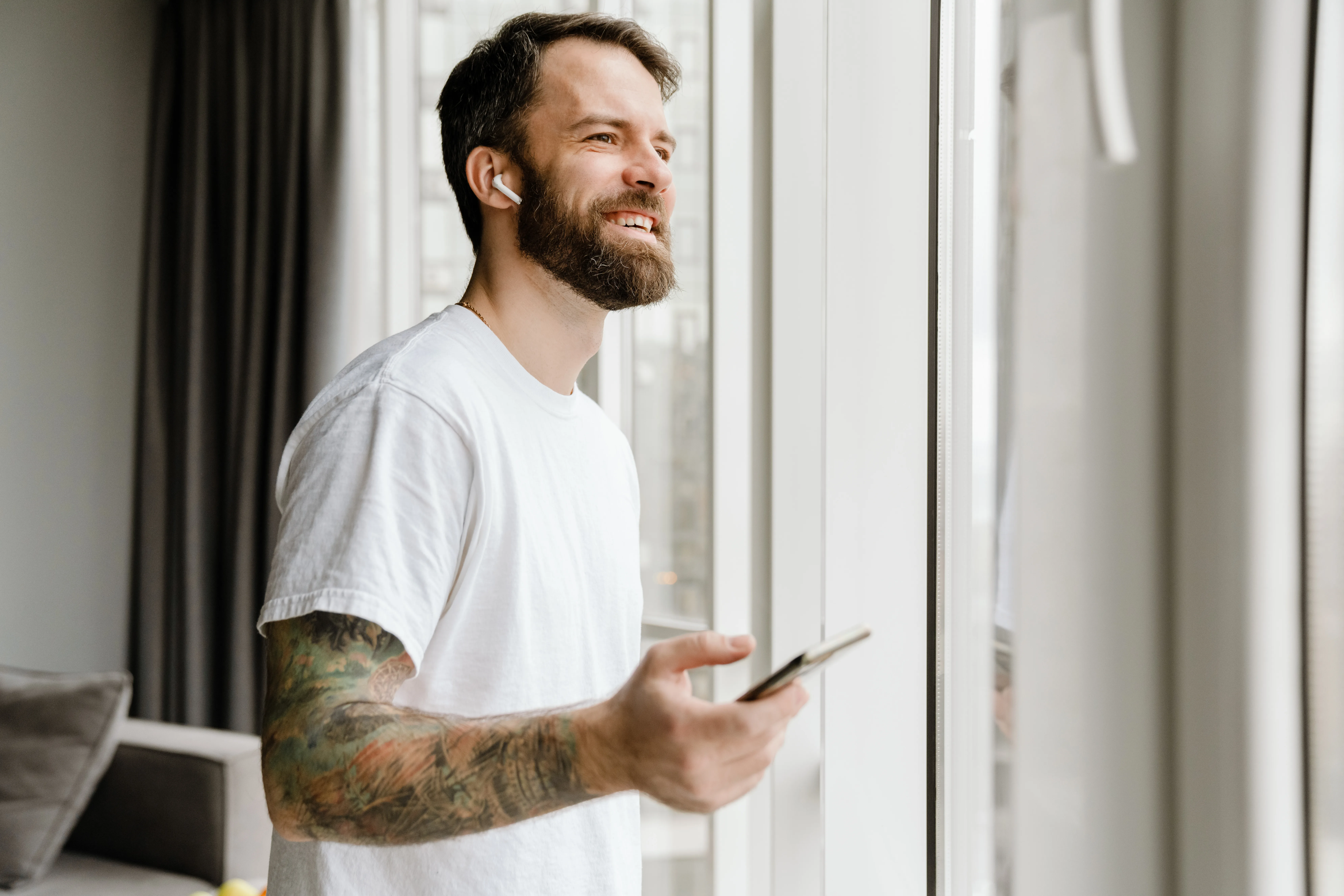Bearded european man smiling while using mobile phone at home