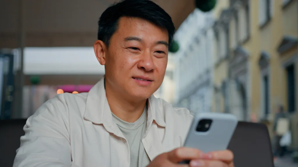 LinkedIn Networking can be done on the go. Image description: Close-up happy asian man holding mobile phone browsing social network male tourist booking ticket