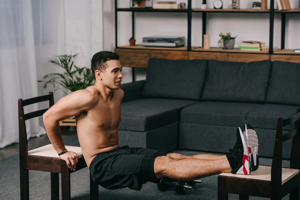 Easy Work-From-Home Exercises. Image description: handsome mixed race man exercising on chairs in apartment